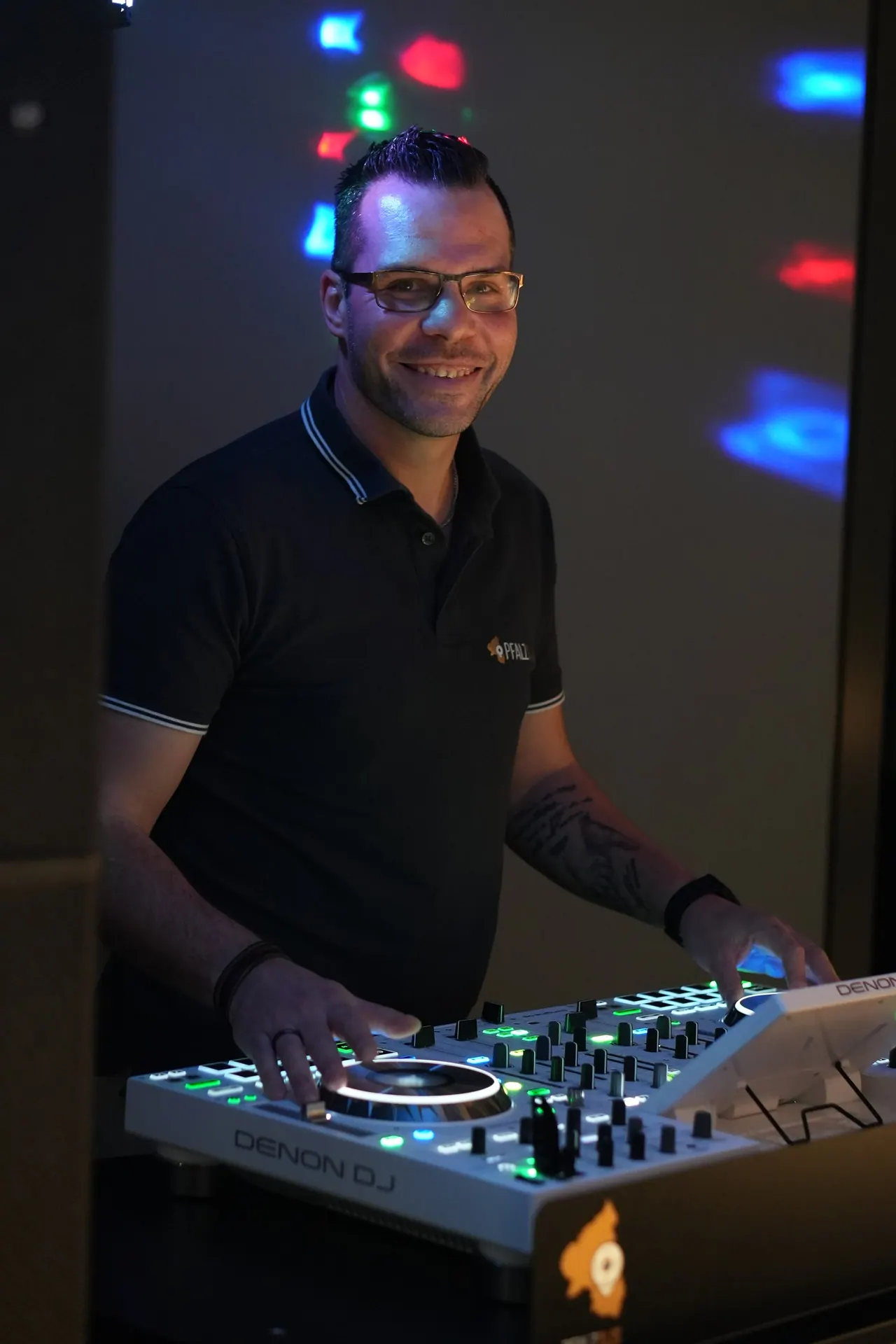 Dominik Hans lächelnd am beleuchteten DJ-Controller, im Hintergrund bunte Lichtpunkte