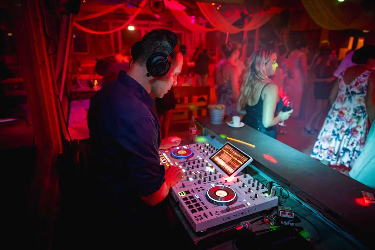 Dominik Hans mit Kopfhörern am DJ-Pult, dahinter feiernde Gäste in rotem Licht
