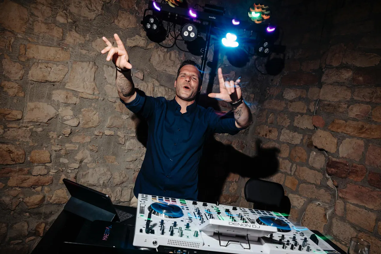 Dominik Hans hinter dem DJ-Pult im Gewölbekeller, beide Arme nach oben gestreckt