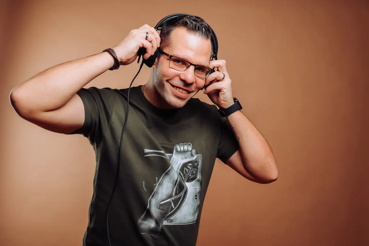Dominik Hans lächelnd mit Kopfhörern vor braunem Studiohintergrund